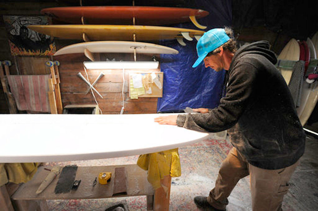 Kyle Shellhammer, owner and shaper for Eggnog Surfboards, works on a surfboard order for a client in his garage, in Coos Bay, Oregon, on Feb. 6. (Bethany Baker /The World via AP)
