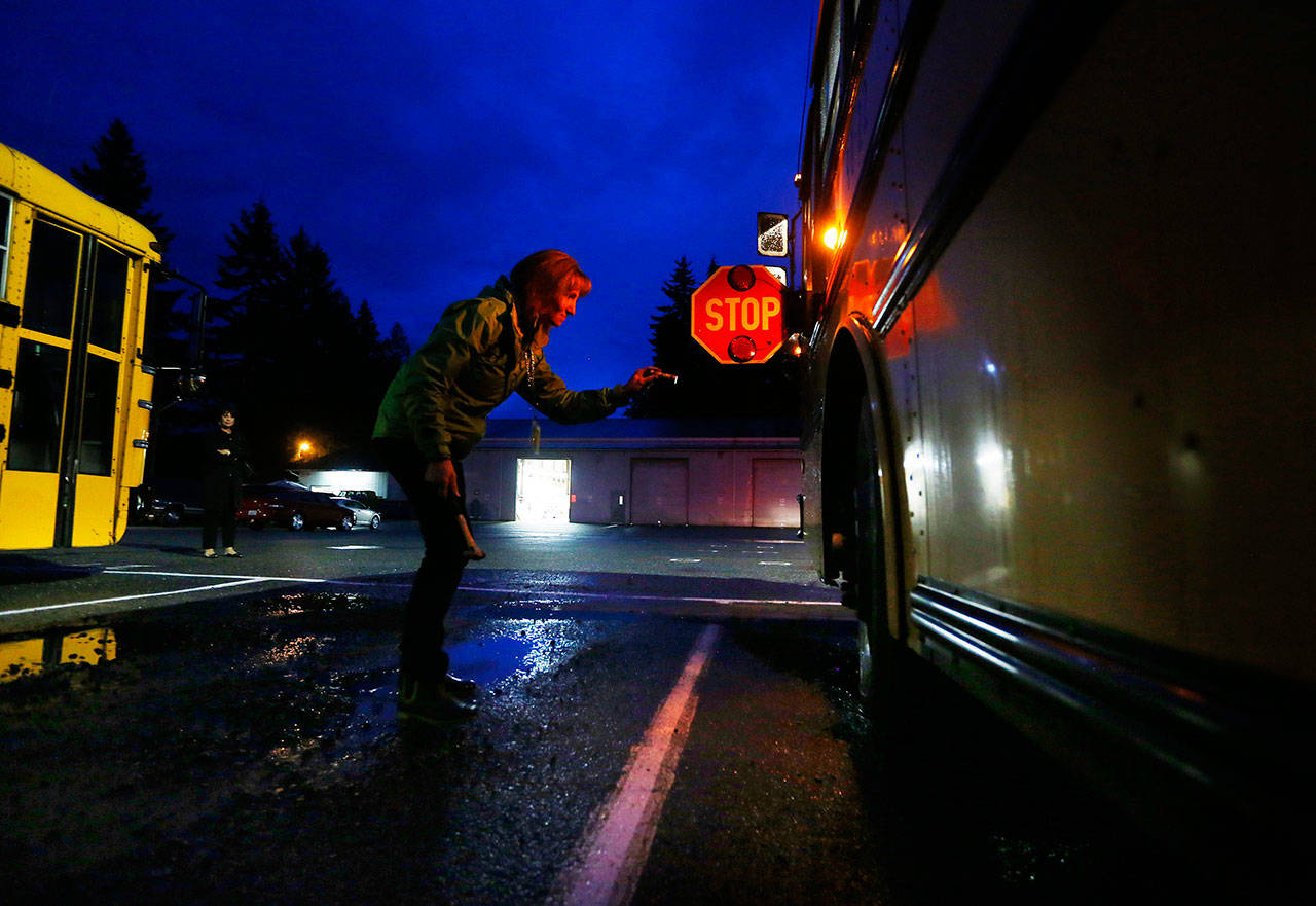 Bus driver Carol Mitzelfeldt checks her school bus, its stop paddle extended, before leaving on her route for the Arlington School District on an October morning in 2014. The Marysville School District recently had cameras installed on 15 of its buses that record the license plates of vehicles that illegally pass stopped buses. Fines are then sent to vehicle owners. (Mark Mulligan / Herald file photo)