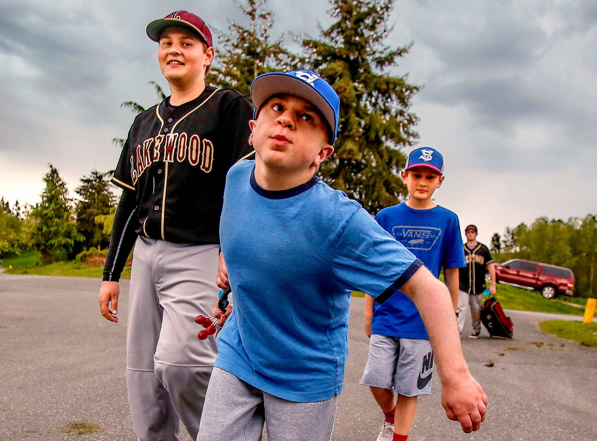 Brothers Matthew Irish, 15 (left), and Noah, 11, follow their older brother, Jacob, 16, as they walk to their car from the baseball field at Lakewood Middle School on Thursday after games were canceled by lightning. Jacob, who was born with life-threatening Hurler syndrome, is playing on a baseball team for the first time. (Dan Bates / The Herald)