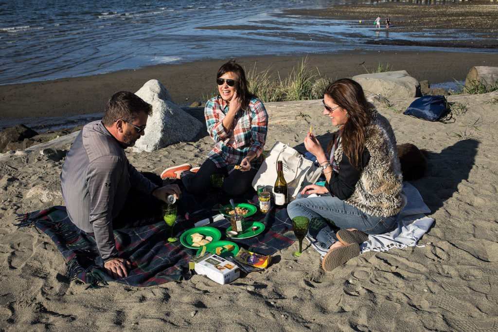 Andrew Gaston, Julissa Downing, and Kelly Colman enjoy a picnic at Edgewater Beach in Mukilteo. Colman owns Proper Picnic, a company that sells ready-to-go picnics. (Andy Bronson / The Herald)
