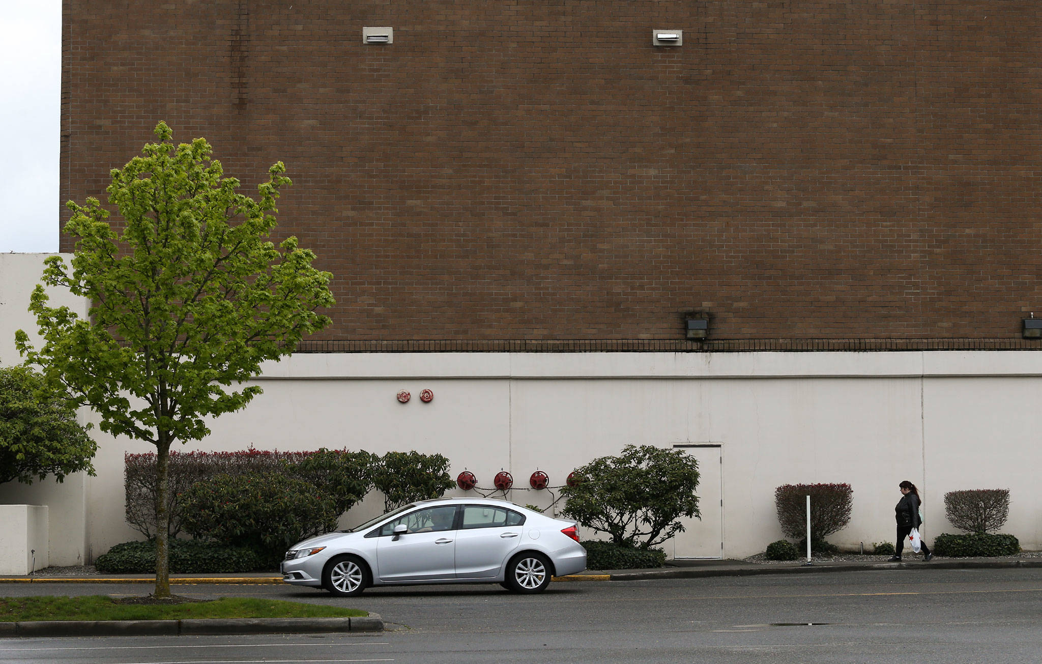 With the former sign taken down, a car and pedestrian walk past the empty Sears building at Alderwood mall on Monday in Lynnwood. (Andy Bronson / The Herald)