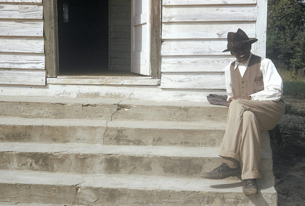 In this 1950s photo, a man included in a syphilis study sits on steps in front of of a house in Tuskegee, Alabama. (National Archive via AP)
