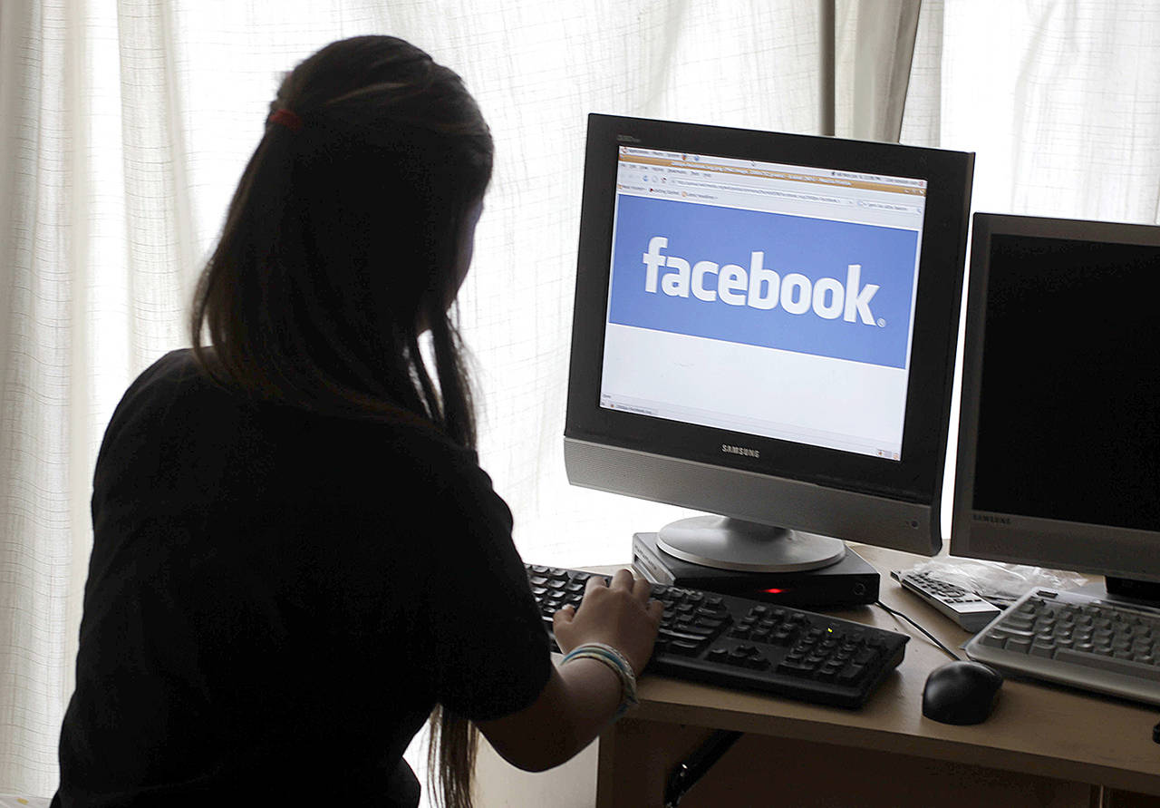 In this 2012 photo, a girl looks at Facebook on her computer in Palo Alto, California. In a blog post Wednesday, May 3, Facebook CEO Mark Zuckerberg said that the company will hire another 3,000 people to review videos of crime and suicides following murders shown live. (AP Photo/Paul Sakuma, File)