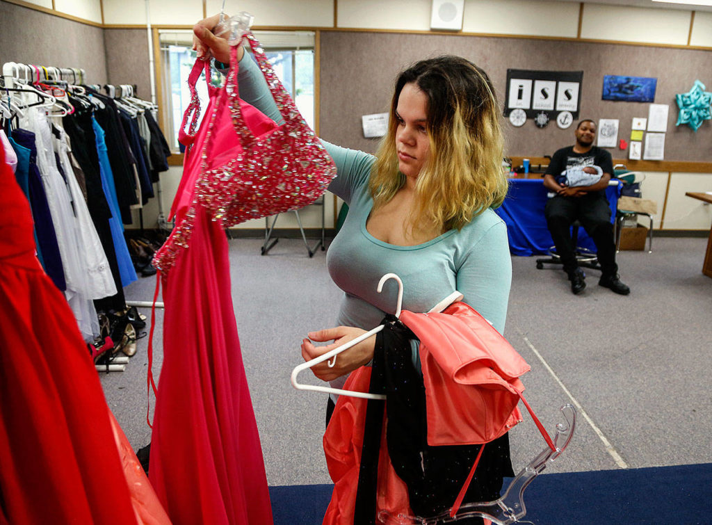 Joslyn Spradley, 18, looks over dresses while her prom date Damion Wilson-Cobbs, 19, holds their month-old son, Avery. (Dan Bates / The Herald)
