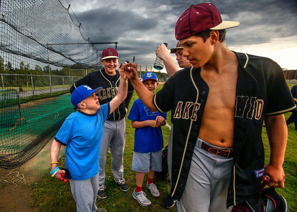 Matthew and Noah Irish look on as Lakewood High School baseball player Morgan Stacey fist-bumps with Jacob Irish as all players leave the fields. (Dan Bates / The Herald)
