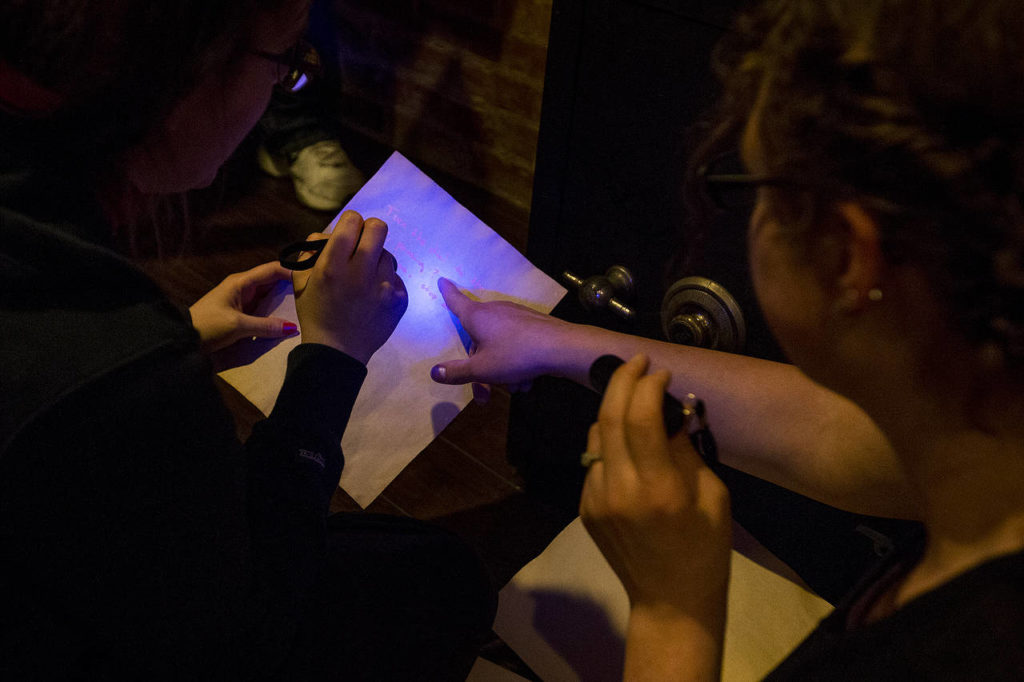 Catherine Harlow (left) and Alicia Flansburg use blacklights to find hidden messages on documents at the new Escape Scene in downtown Everett on May 6. (Ian Terry / The Herald)
