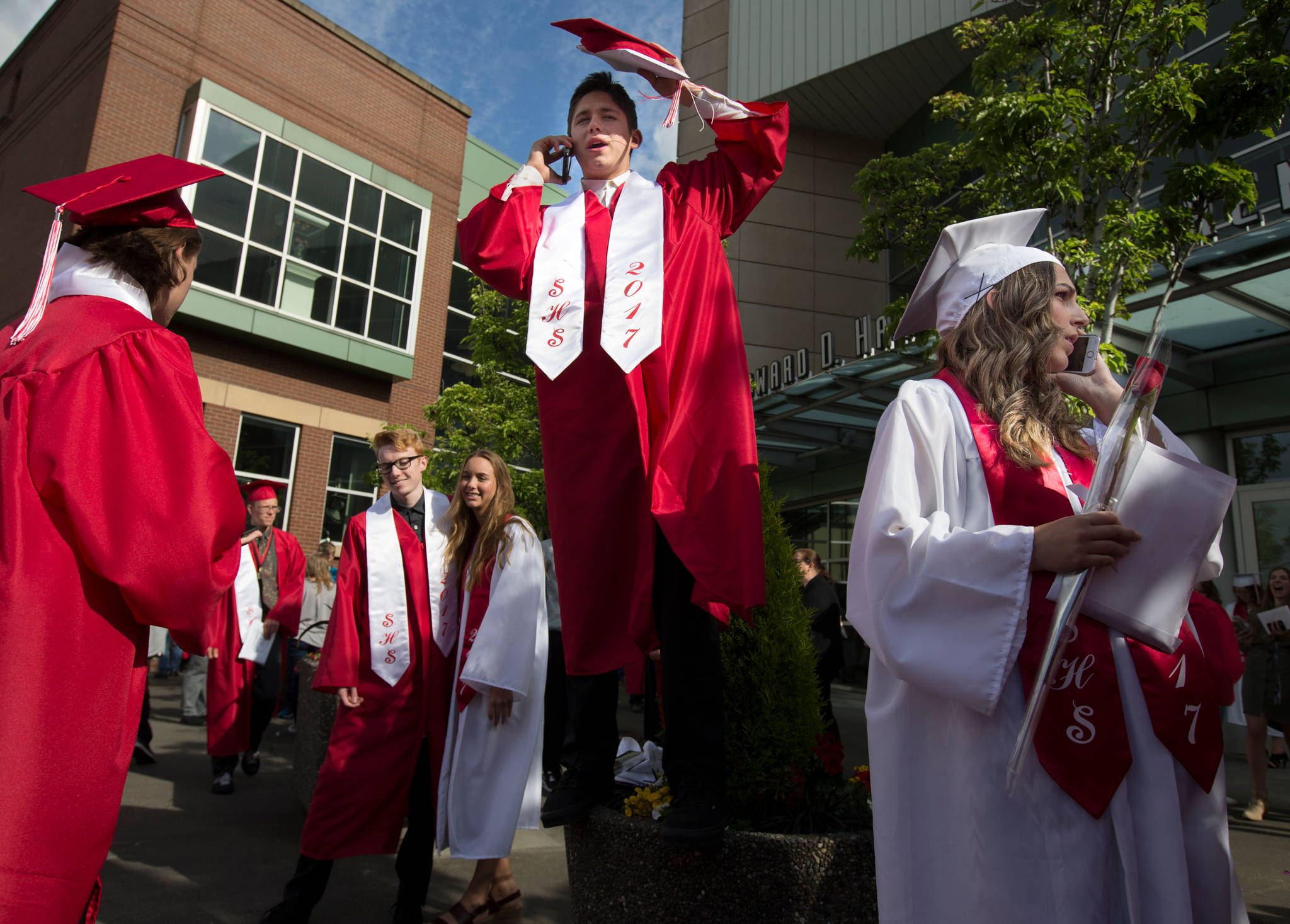 Snohomish High graduate Riley Gagnon (center) finds tries to get a better view to find his family as Analise Bingham (right) calls on the phone after their graduation ceremony at Xfinity Arena on Monday in Everett. (Andy Bronson / The Herald)