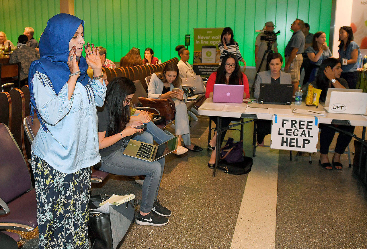 While activists and lawyers at the table at right offer help and information, Hanadi Al-Haj prays in the Tom Bradley International Terminal at Los Angeles International Airport as she waits for her Yemeni mother to arrive from Jordan via Istanbul, on Thursday. (AP Photo/Mark J. Terrill)