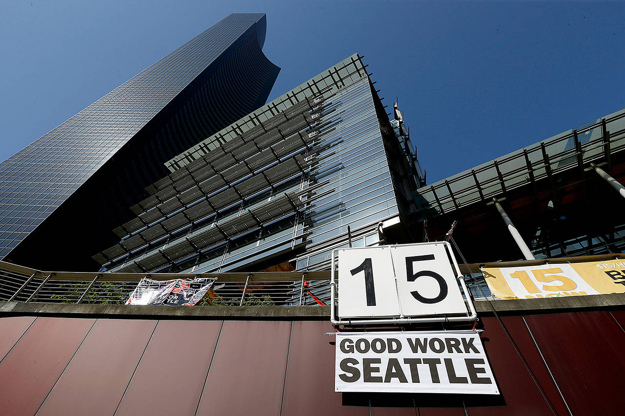 A sign that reads “15 Good Work Seattle” is displayed below Seattle City Hall (right) and the Columbia Center building (left) after the Seattle City Council passed a $15 minimum wage measure in 2014. (AP Photo/Ted S. Warren, File)