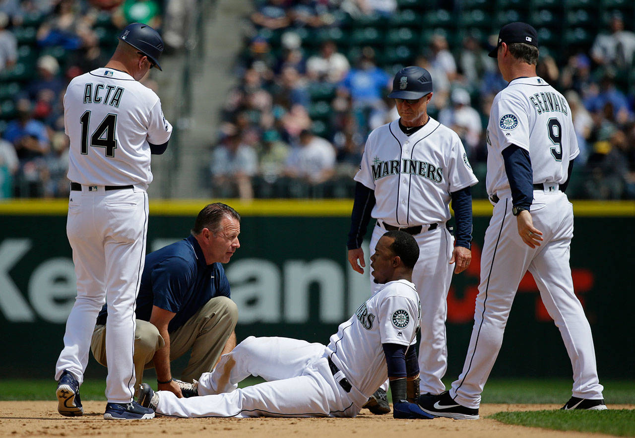 Mariners shortstop Jean Segura (bottom) is examined by trainer Rob Nodine after suffering an injury sliding into second base in the fourth inning of a game against the Rockies on June 1, 2017, in Seattle. (AP Photo/Ted S. Warren)