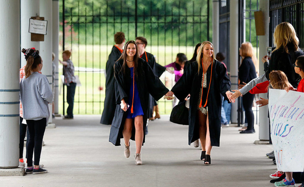 Graduating seniors Mya Dennis (left) and Ashly Walker hold hands and lead fellow graduates around the Chain Lake Elementary School campus Friday, in the school’s first-ever “senior walk.” (Dan Bates / The Herald)
