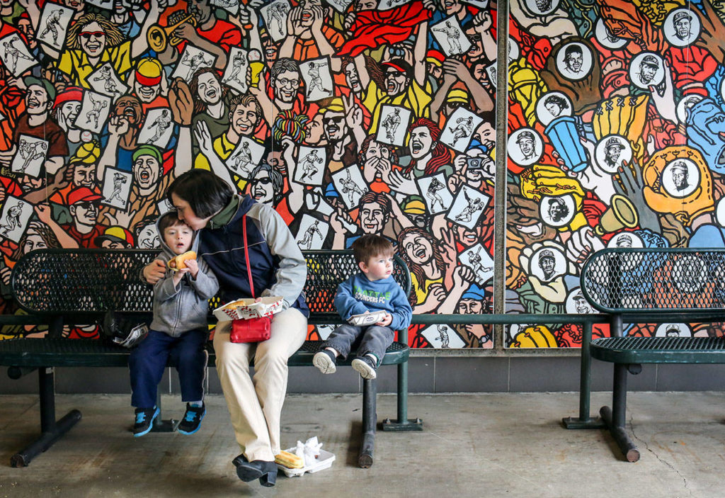 Ransom Butaud (left), his mother, Eleya Butaud, and brother, Sam Butaud, enjoy the sights and sounds of the concourse in front of a 24-foot long porcelain enamel mural called “The Crowd.” (Kevin Clark / The Herald)
