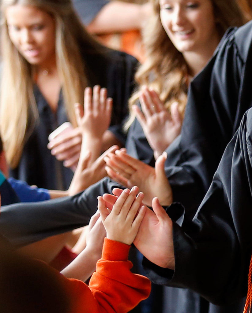 Monroe High School graduating seniors touch hands with young students as they pass through a gauntlet of Chain Lake Elementary kids Friday in a first-ever “senior walk” for the school. (Dan Bates / The Herald)
