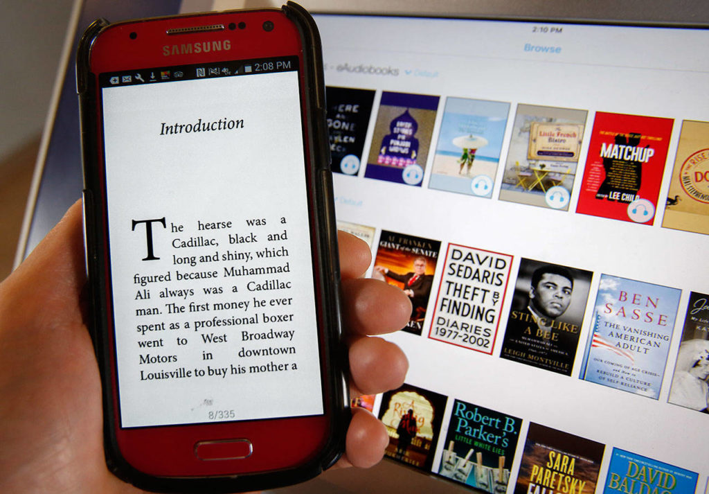 The opening page of “Sting Like a Bee,” a Muhammad Ali biography, shows on the cellphone of a user of the Cloud Library ebook kiosk recently installed at Everett Station. The Everett Public Library’s kiosk is available for anyone to use without charge. In the background are images of books available on the kiosk, including “Sting Like a Bee.” (Dan Bates / The Herald)
