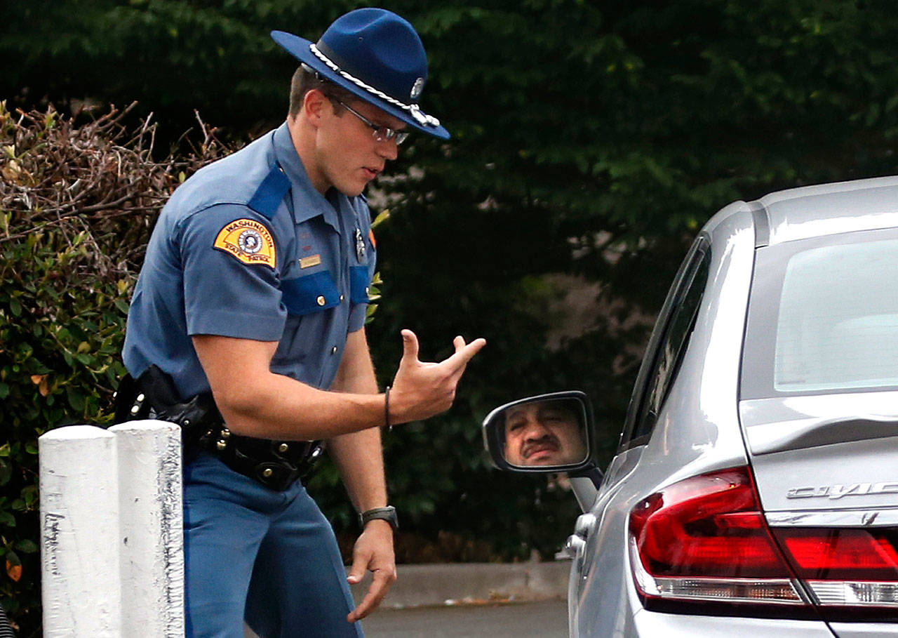 Washington State Patrol Trooper Mark Francis demonstrates to a driver, how he was holding a cell phone while driving, near Smokey Point in 2015. Starting July 23, drivers can be cited for distracted driving for holding a cellphone for talking, texting and other uses. Hands-free devices are allowed. (Dan Bates / Herald file photo)
