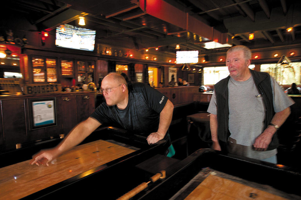 Celebrating his 50th birthday, Mark Rice (left) and his father-in-law, Ed Ness, play shuffleboard in the Woodshed bar at McMenamins Anderson School on March 8 in Bothell. (Andy Bronson / The Herald)
