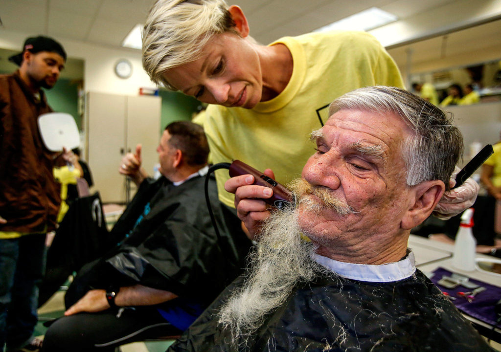 After giving him a haircut Thursday, Paroba College of Cosmetology and Barbering student Sommer McKenzie removes the full beard, along with some years, from the face of Rick Young, who has been staying at the Everett Gospel Mission the past month. In the background, fellow student Davonte Peterson holds a mirror for Matthew Clark, 50, who gives a thumbs up to the new haircut. (Dan Bates / The Herald)
