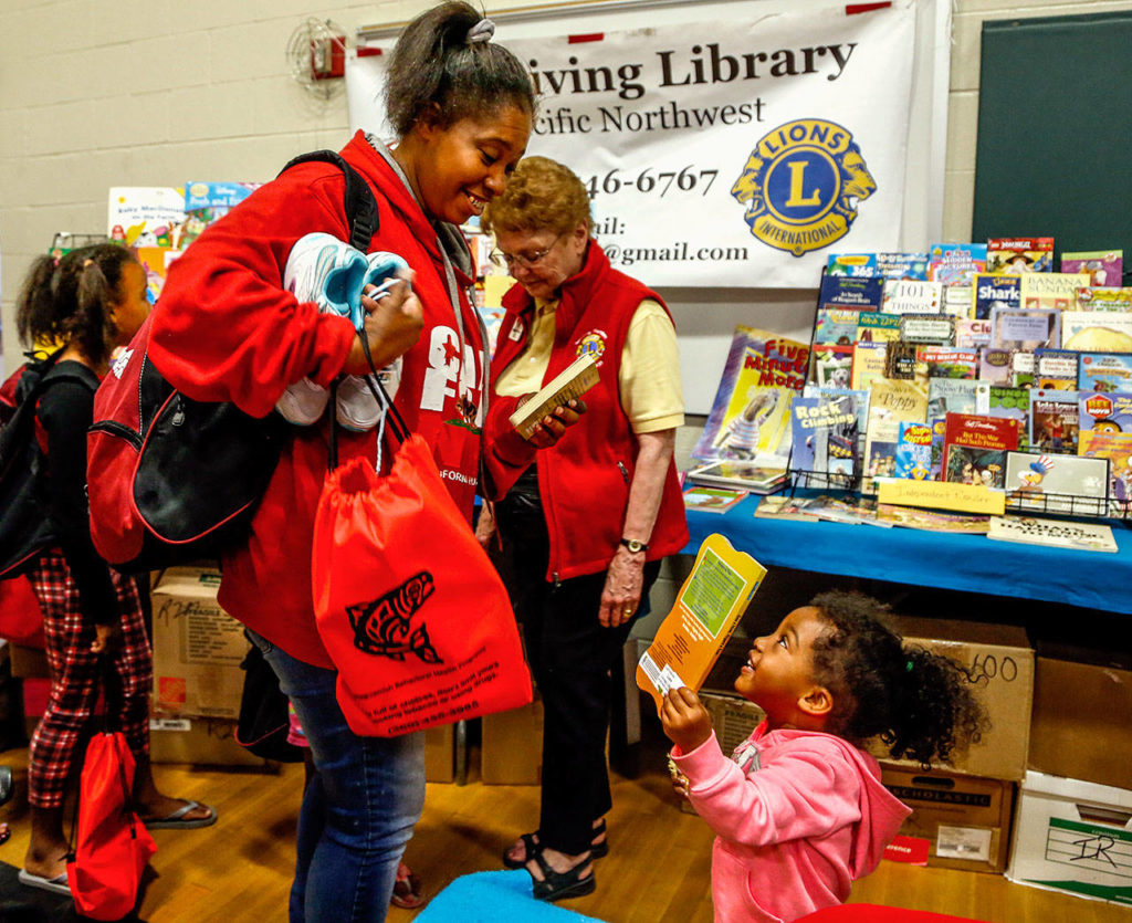 Meka Laird, 40, helps her 2-year old daughter, Destiny, pick out a book called “Eyes and Nose, Fingers and Toes” from the Lions Giving Library at Project Homeless Connect. Laird, of Marysville, is a mother of eight who also has one grandson. Her biggest need Thursday was school supplies. (Dan Bates / The Herald)
