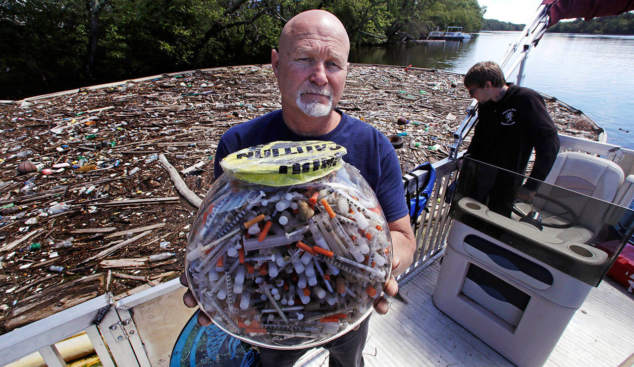 Rocky Morrison, of the “Clean River Project”, holds up a fish bowl filled with hypodermic needles, that were recovered during 2016, on the Merrimack River next to their facility June 7, in Methuen, Mass. A cleanup effort along the Merrimack River, which winds through the old milling city of Lowell, has recovered hundreds of needles in abandoned homeless camps that dot the banks, as well as in piles of debris that collect in floating booms he recently started setting. (AP Photo/Charles Krupa)