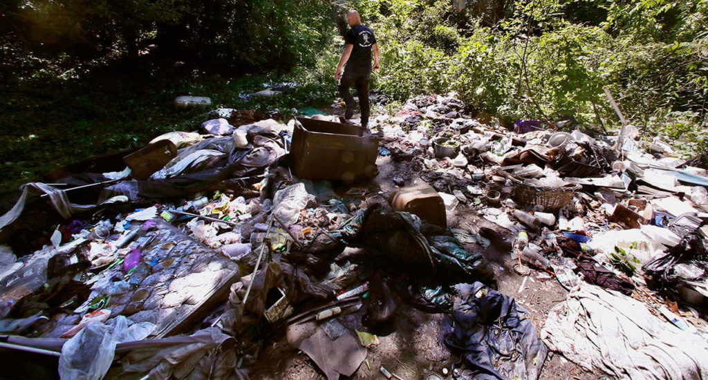 In this Wednesday June 7, 2017 photo, activist Rocky Morrison walks through an encampment where opioid addicts shoot up along the Merrimack River in Lowell, Mass. Morrison leads a cleanup effort along the Merrimack River, which winds through the old milling city of Lowell, and has recovered hundreds of needles in abandoned homeless camps that dot the banks, as well as in piles of debris that collect in floating booms he recently started setting. (AP Photo/Charles Krupa)
