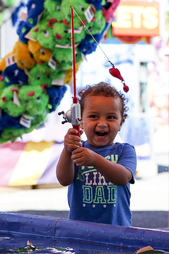 Zeke Tesfaye, 2, laughs as he plays a fishing carnival game during the first day of Aquafest in downtown Lake Stevens on Friday. Tesfaye just immigrated to the U.S. from Ethiopia in March and was brought to the festival by his grandmother, Carrie Thompson. (Ian Terry / The Herald)
