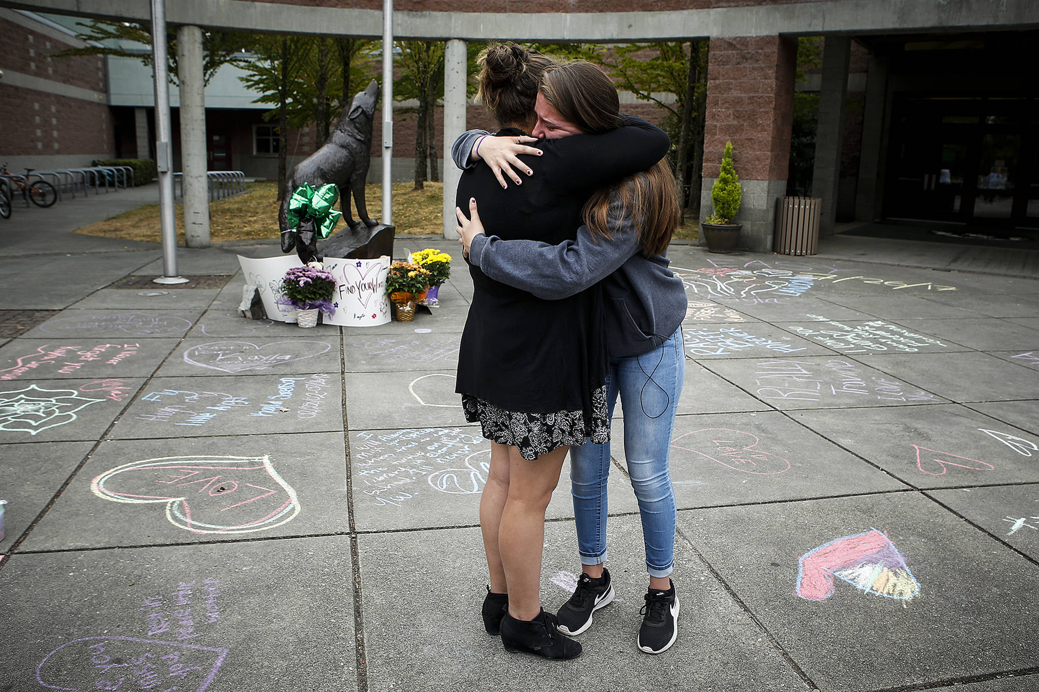 Friends Mariela McNeal (left), 15, and Lauren Crossley, 14, hug near the entrance of Jackson High School where friends and family gathered Thursday to write messages of remembrance for three teens killed in a car crash in Lynnwood early Wednesday. All three who were killed were students at Jackson High School. (Ian Terry / The Herald)
