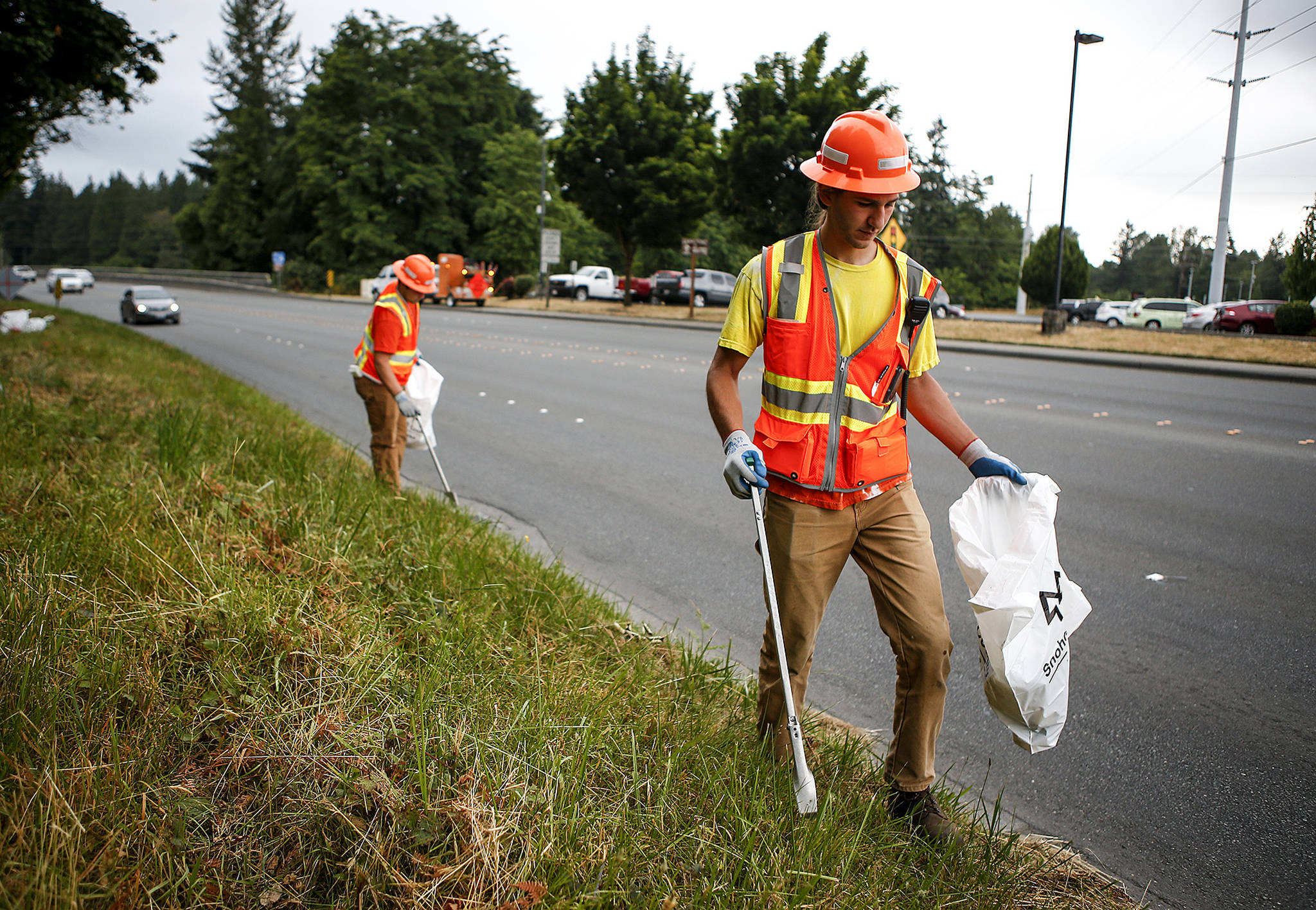 Seasonal Snohomish County workers Kyle Schuman (right) and Dakota Scherrer pick up trash along Marine Drive in Marysville on June 28. (Ian Terry / The Herald)