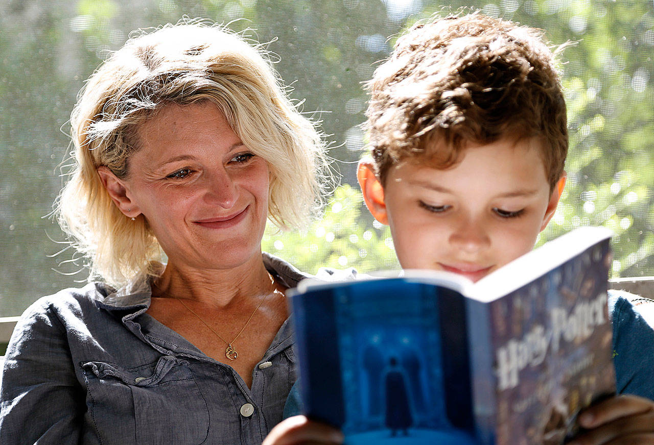 Theo Galkin, 8, rereads a favorite part of “Harry Potter and the Sorcerer’s Stone” while posing for a picture with his mother Chloe Galkin at their home in South Orange, New Jersey. As the 20th anniversary of the initial publishing of the first Harry Potter book is celebrated this week, another generation is being introduced to Harry, Hogwarts and all the rest of the magical world created by author J.K. Rowling. (AP Photo/Seth Wenig)