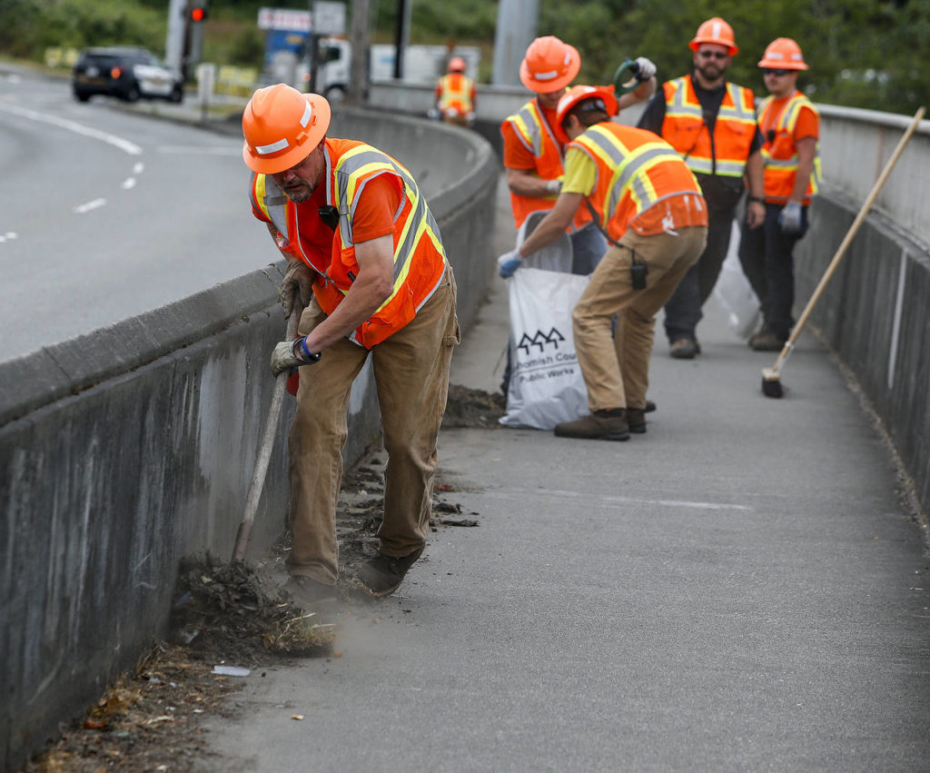 Snohomish County workers clean a sidewalk of trash and debris along Marine Drive in Marysville on June 28. (Ian Terry / The Herald)
