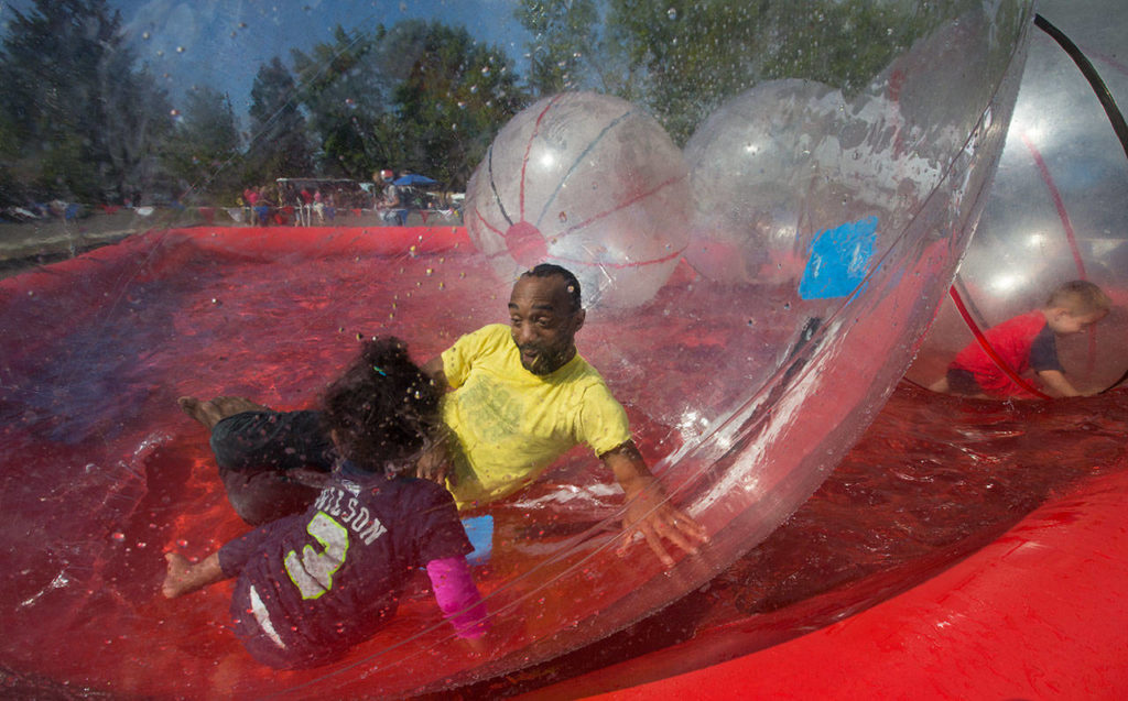 Bernard Georges and his daughter, Daphne, 2, play in waterballs at the Mountlake Terrace 3rd of July event at Ballinger Park on Monday. (Andy Bronson / The Herald)
