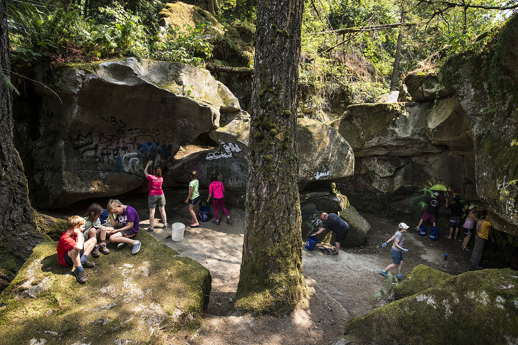 Volunteers use brushes and scrapers to remove graffiti from rocks at Eagle Falls near Index on Saturday, Aug. 5. (Ian Terry / The Herald)