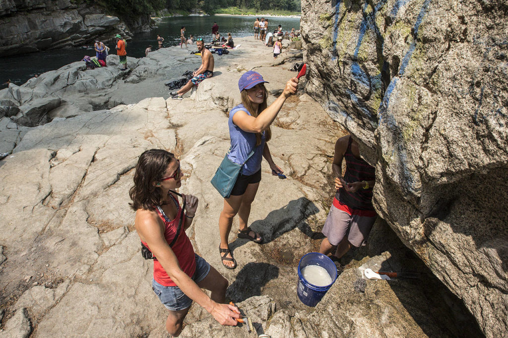 Ally Hinds (center) scrubs away graffiti along with friends Katie Heard (left) and Janelle Dean at Eagle Falls near Index on Saturday, Aug. 5. (Ian Terry / The Herald)
