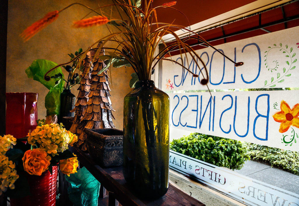 A few items stand ready for sale on shelves behind “Closing Business” posters in the display window of longtime neighborhood store Flowers by Adrian at 2101 Colby Ave. in Everett this week. (Dan Bates / The Herald)
