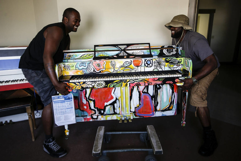 Alton Johnson (left) and KJ Butler, movers from The Piano & Organ Moving Company, hoist a piano up before delivering it to its final location in downtown Everett on Wednesday, Aug. 2. (Ian Terry / The Herald)
