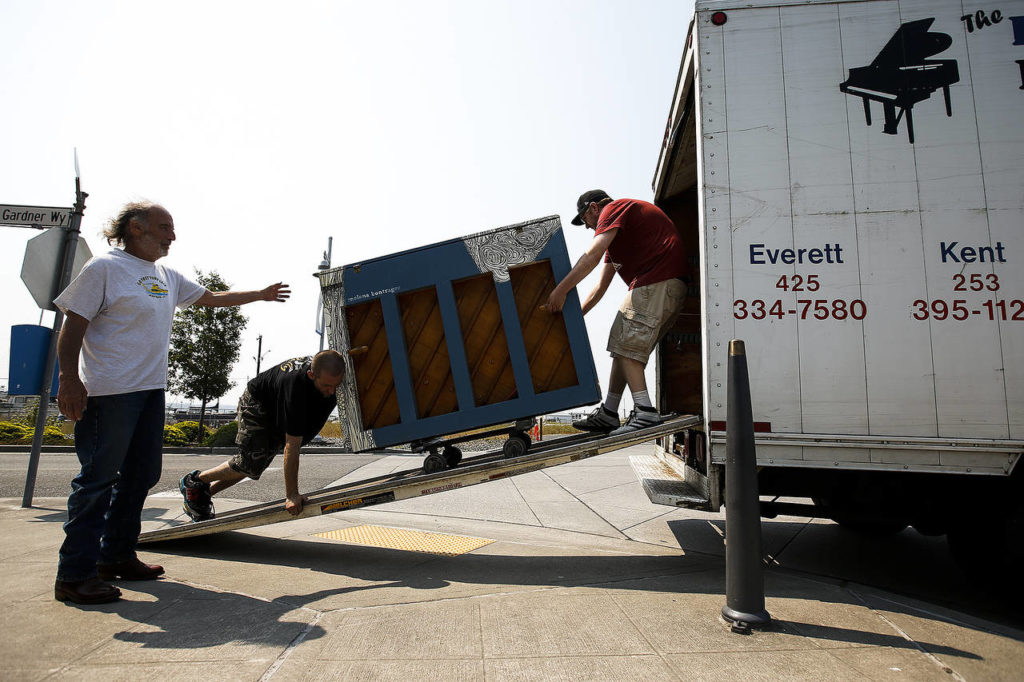 Mike Alkire (left) directs Dan Demascio (center left) and Robert Alkire as they roll out a piano to be placed in front of Scuttlebutt Brewery on the Everett waterfront on Wednesday, Aug. 2. (Ian Terry / The Herald)
