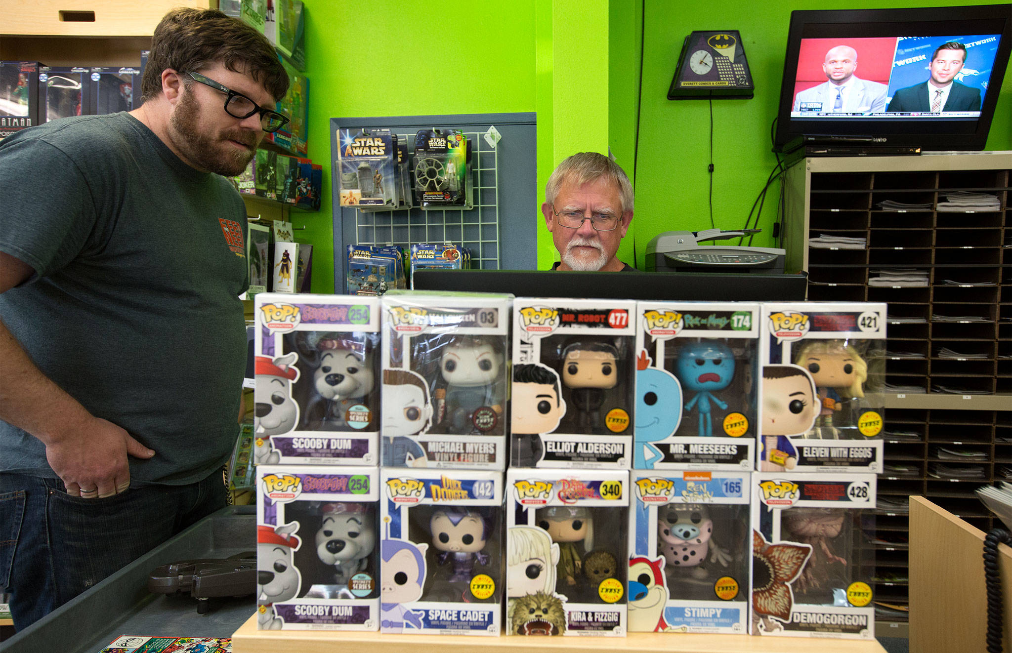 Behind rows of Funko Pop! figures, owner Charlie Knoedler looks up comic book information for Christian Holst at Everett Comics on Wetmore Avenue. Funko is moving its headquarters and a store across the street from the long-time comic shop. (Andy Bronson / The Herald)