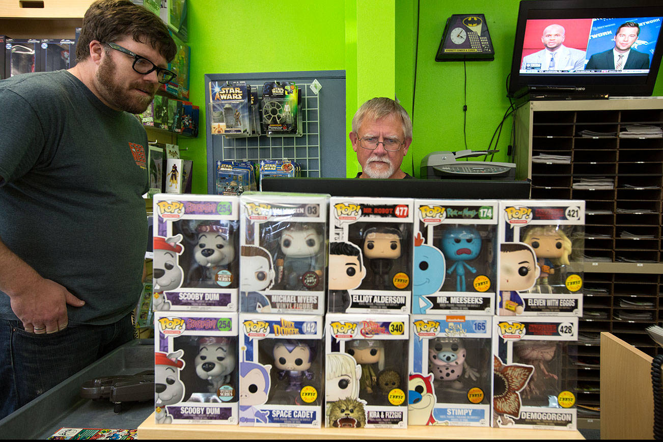 Behind rows of Funko Pop! dolls, Charlie Knoedler looks up comic book information for Christian Holst at Everett Comics, their store, on Wetmore Avenue on Tuesday, July 11, 2017 in Everett. Funko’s presence nearby may affect their bottom line as they sell Funko characters and it makes up 15 to 20 percent of their income. (Andy Bronson / The Herald)