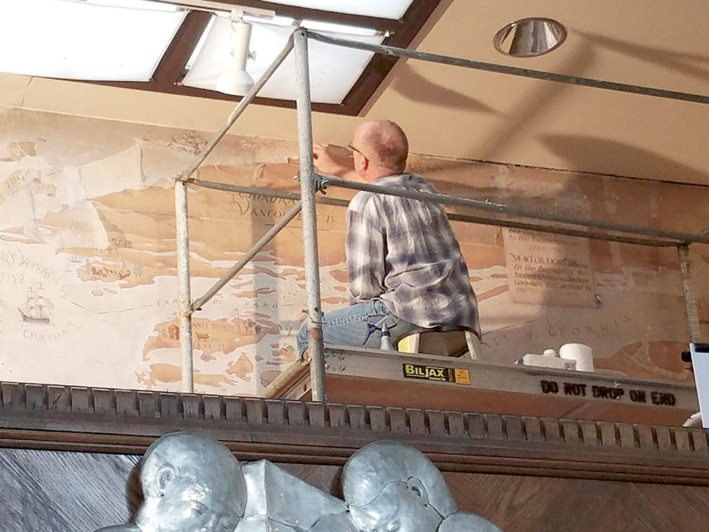 Peter Malarkey works on restoring Everett Library’s J. T. Jacobsen murals. (Lisa Labovitc / Courtesy of Everett Public Library)
