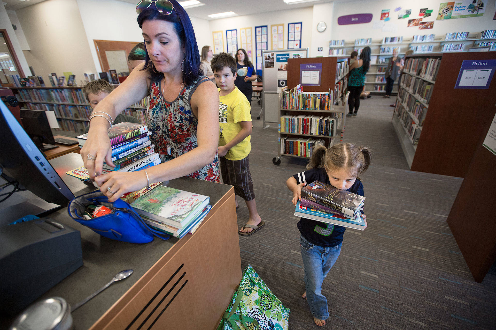 As her mother, Ande, looks for her library card, Magdalena Gaiten, 5, carries a heavy load of books to the checkout counter at Mariner Library on Monday in Everett. The family of four kids checked out 27 books from the library, which they visit weekly. (Andy Bronson / The Herald)