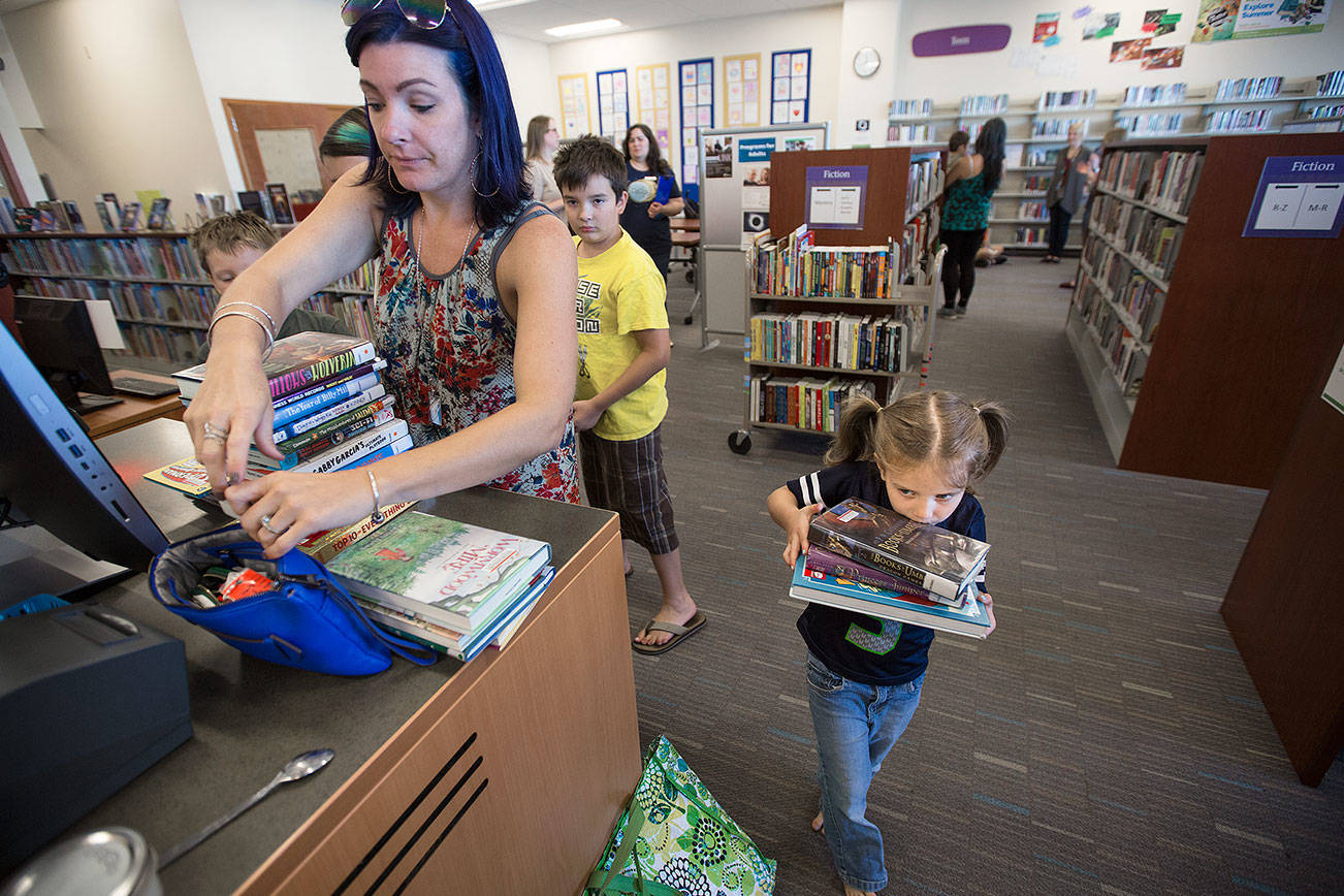 As her mother Ande looks for the library card, Magdalena Gaiten, 5, carries a heavy load of books to the checkout counter at Mariner Library on Monday, Aug. 21, 2017 in Everett, Wa. The family of four kids checked out 27 books from the library where they make a trip weekly for new books.(Andy Bronson / The Herald)