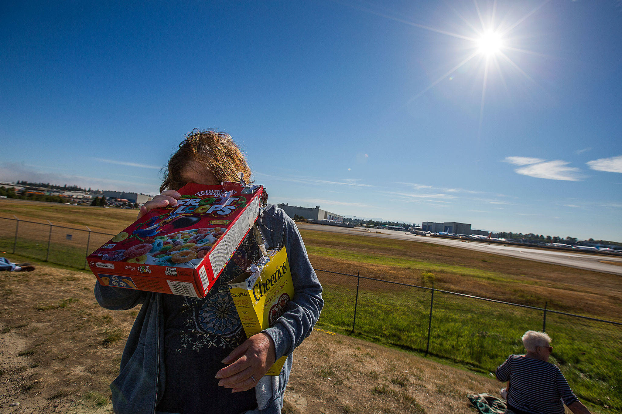 Nancy Sharlin uses one of two cereal boxes to catch a pinhole view of the eclipse along a berm at the Future of Flight Aviation Center on Monday in Mukilteo. (Andy Bronson / The Herald)