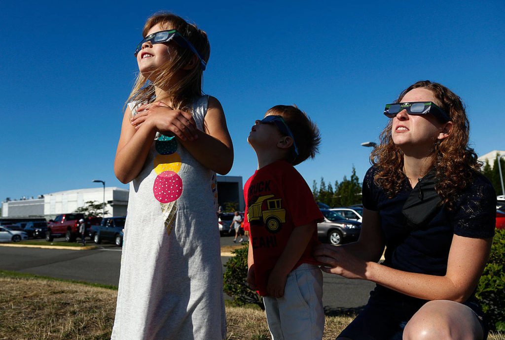 Andrea Nicolayeff (right) and her kids, Avery (left), 6, and Nicolas, 3, get a good look at the solar eclipse outside the Future of Flight and Aviation Center at Paine Field on Monday. (Dan Bates / The Herald)
