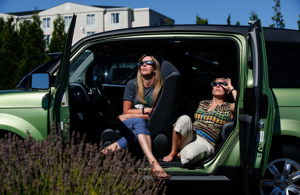 Shellie Rowe (left) and Ann Panozzo, both of Everett, relax in the comfort of their vehicle while watching the solar eclipse from the parking lot outside the Future of Flight Aviation Center at Paine Field in Mukilteo on Monday. (Dan Bates / The Herald)
