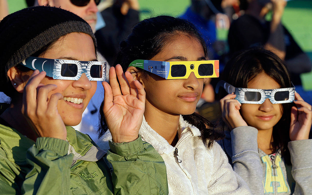 From lefrt, Schweta Kulkarni, Rhea Kulkarni and Saanvi Kulkarni, from Seattle, try out their eclipse glasses at a gathering of viewers in Salem, Oregon, early Monday. (AP Photo/Don Ryan)