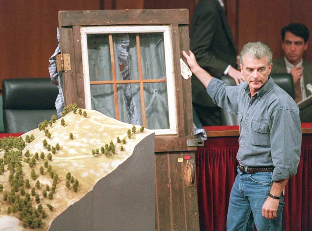 In this Sept. 6, 1995 photo, Randy Weaver holds the door of his cabin showing holes from bullets fired during the 1992 siege of his Ruby Ridge, Idaho home and a model of the landscape during testimony before the Senate Judiciary Subcommittee on Capitol Hill in Washington. (AP Photo/File, Joe Marquette, File)
