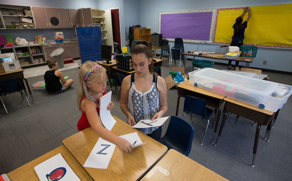 Volunteer Lorin Lawrence helps Kelsey Coggins, 6, sort ABC signs for one of the classrooms. (Andy Bronson / The Herald)
