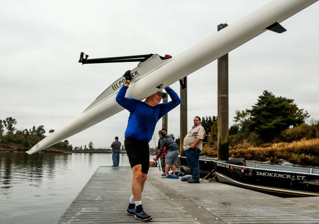 A fisherman nearby watches as Bill Jaquette carries his racing shell to the shell house. (Dan Bates / The Herald)
