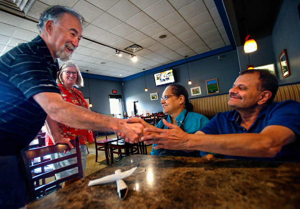 As Linda Witter and Ruqayya Bala enjoy the moment, Bill Witter (left) heartily shakes hands with Shabbir Bala while congratulating him on his retirement and the closure of Boondockers in Marysville Wednesday. (Dan Bates / The Herald)
