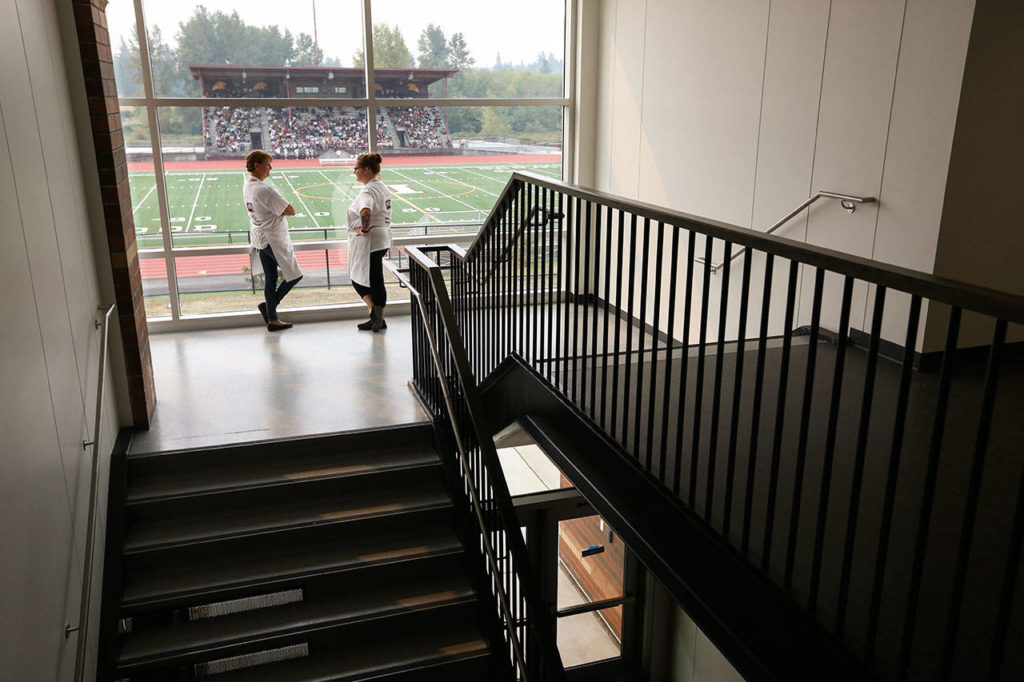 As students sit out on the football bleachers during orientation, kitchen staffers Laura Cannon (left) and Kari Albin chat in a stairway. (Andy Bronson / The Herald)
