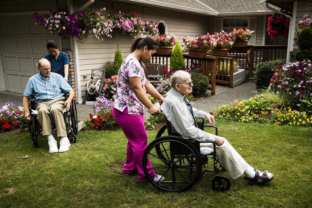 After viewing the hundreds of flowers blooming outside Golfview adult home, Daryl Finley (right), is wheeled through the front lawn by caregiver Marissa Antipolo along with fellow resident Lorne and caregiver Mae Arsulo. (Ian Terry / The Herald)
